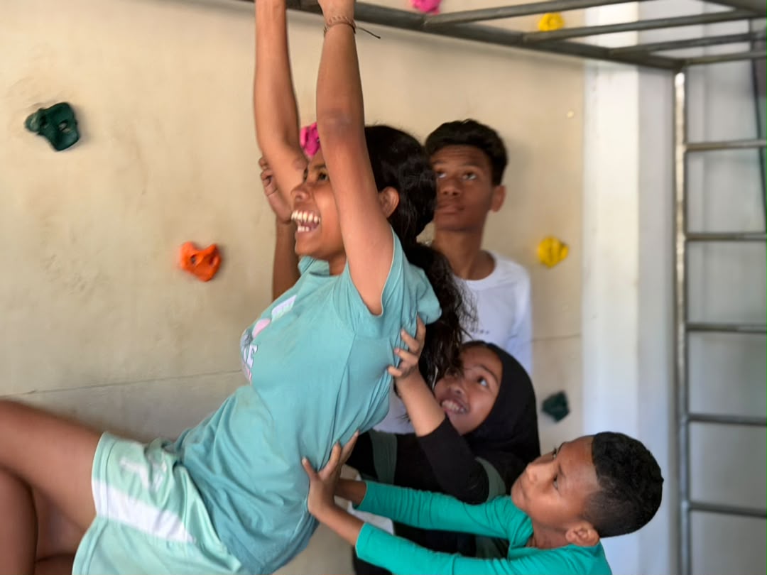 Students helping each other climb a climbing wall at school camp